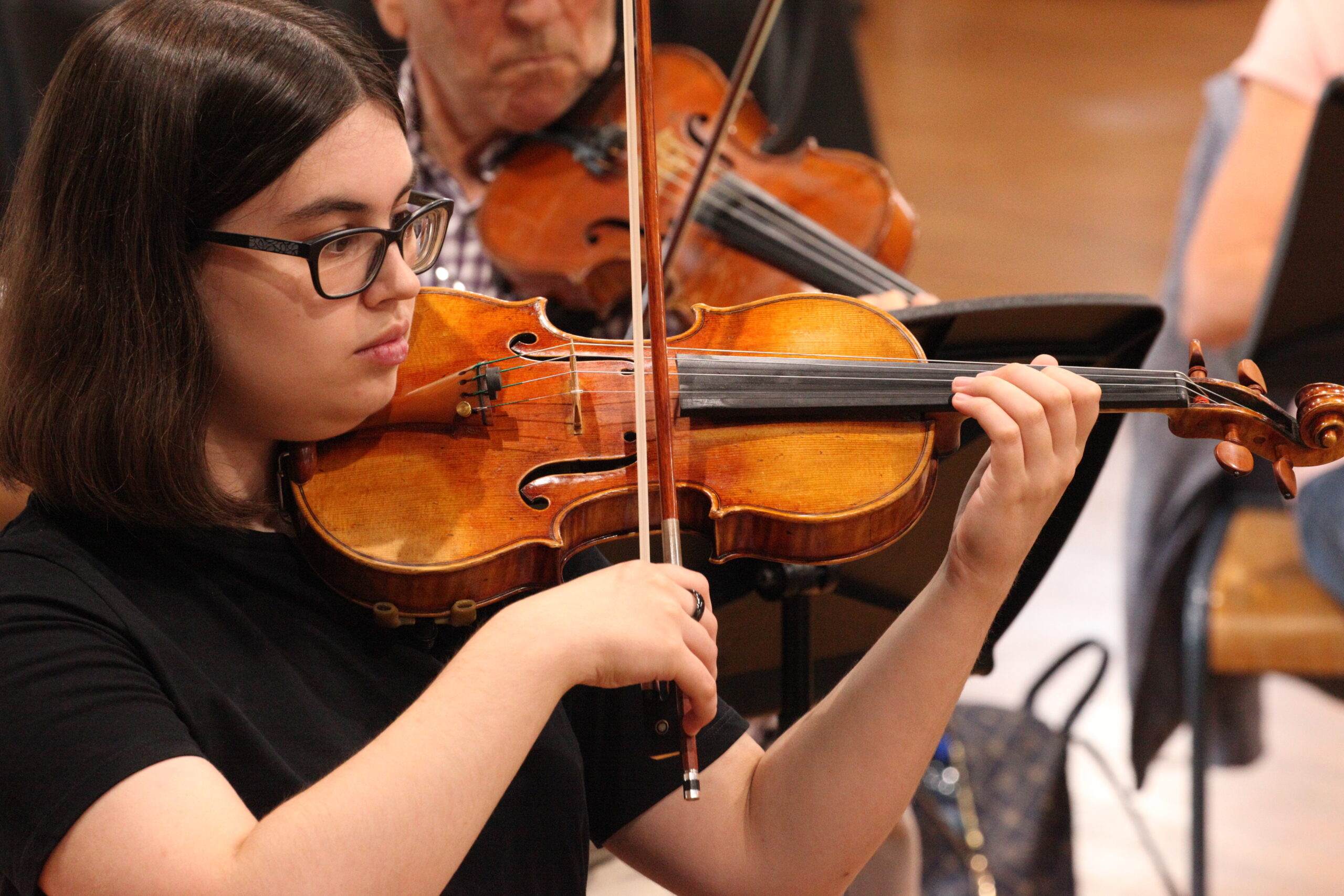 A violin student in the orchestra, playing with focus and poise.