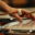 A close-up of a timpanist's hand, muting the skin whilst holding a mallet, the other mallet poised to strike again. Light reflect off the instrument.