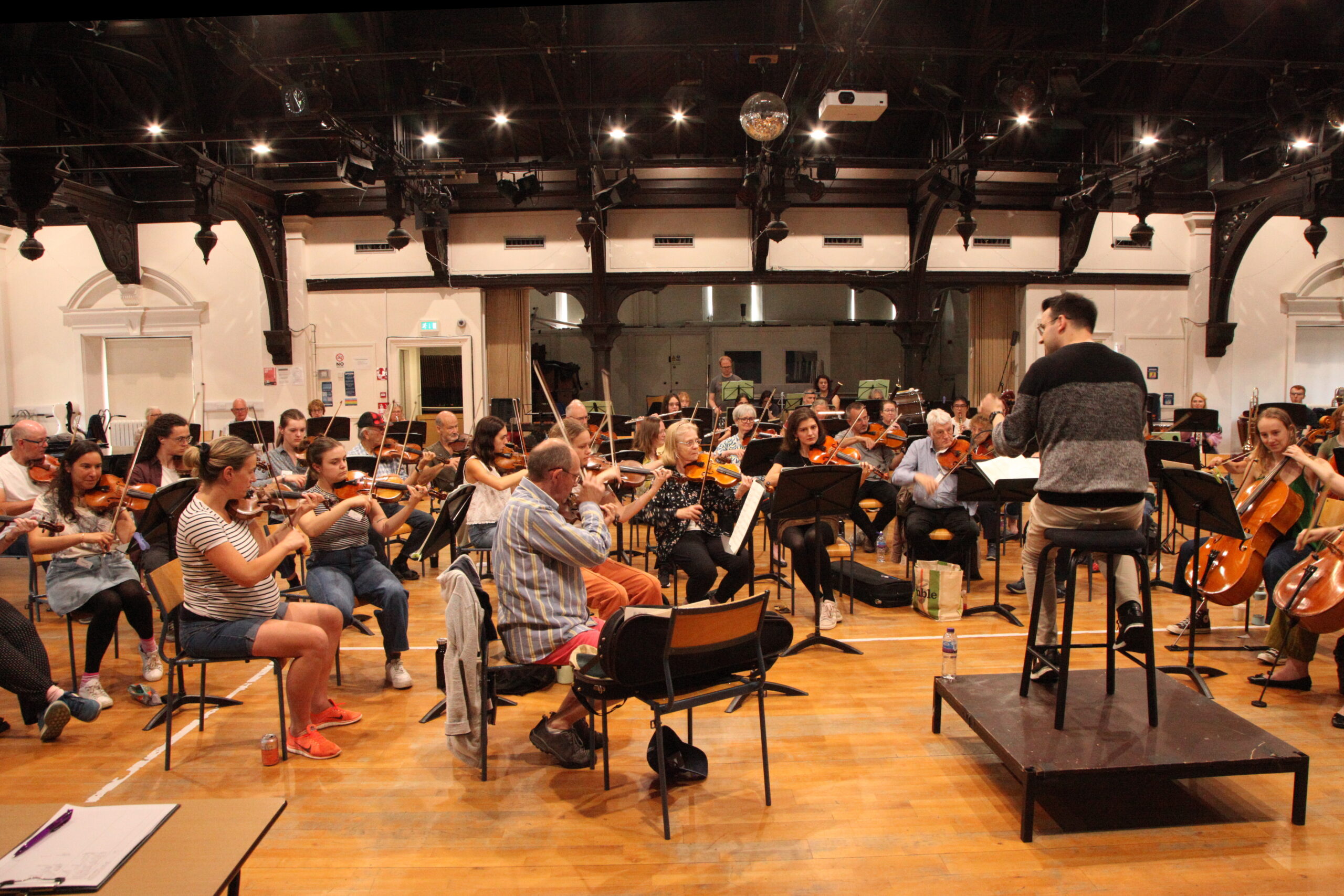 An orchestra in rehearsal, viewed from next to the leader and conductor.