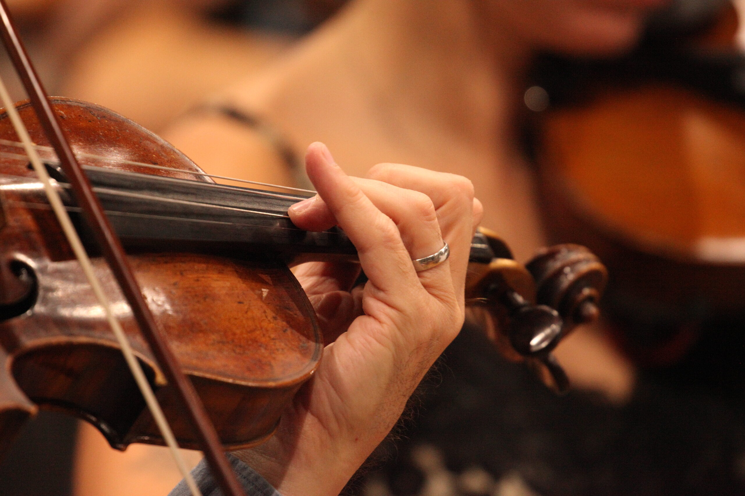 A close-up of a violinist's hand on the fingerboard, fingers pressing down on strings and little finger pointing up.